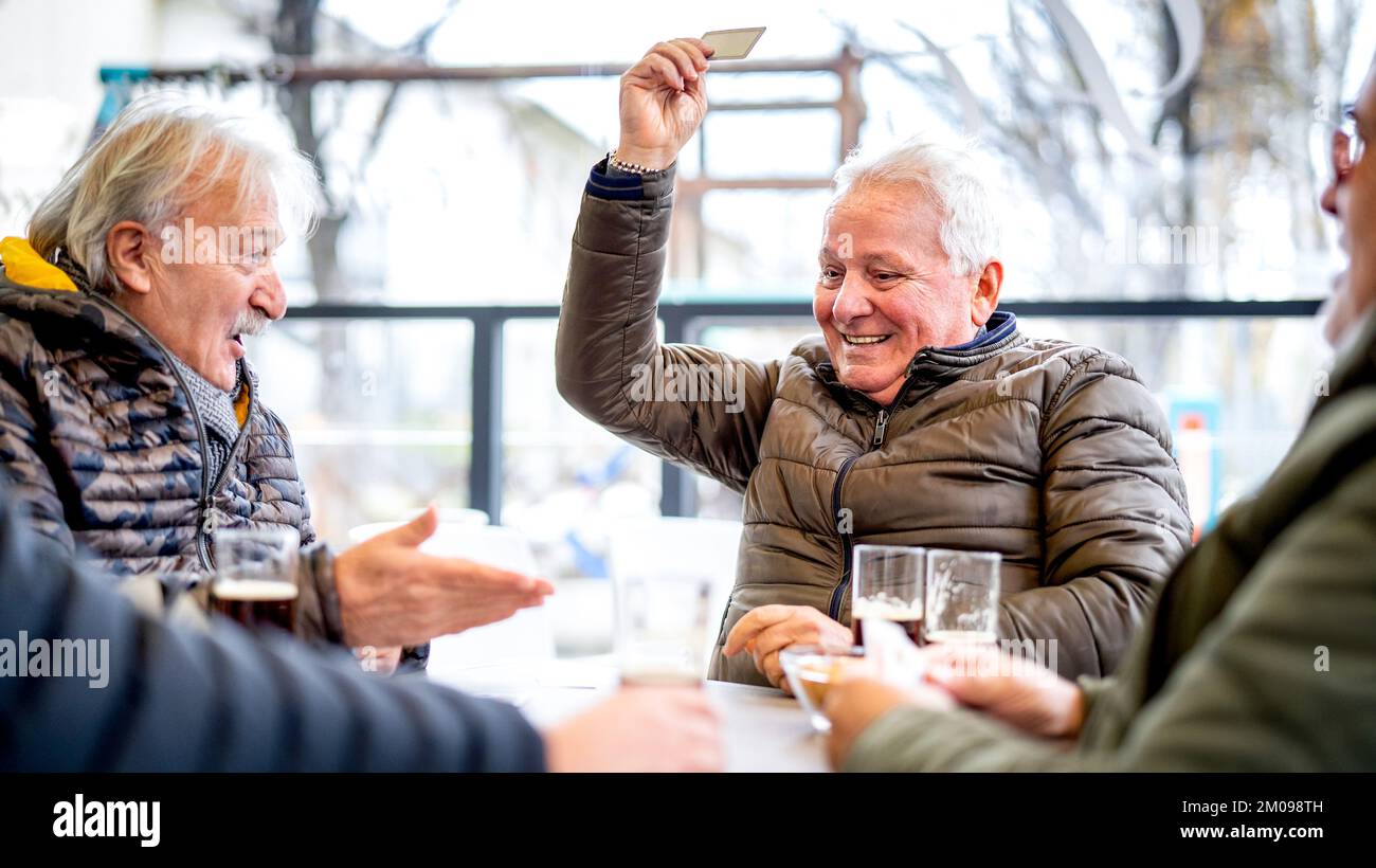 Seniorenfreunde spielen am Wintertag in der lokalen Bar Karten - Ageless Life Style Konzept mit erwachsenen Leuten, die Spaß zusammen haben - heller Kontrastfilter Stockfoto