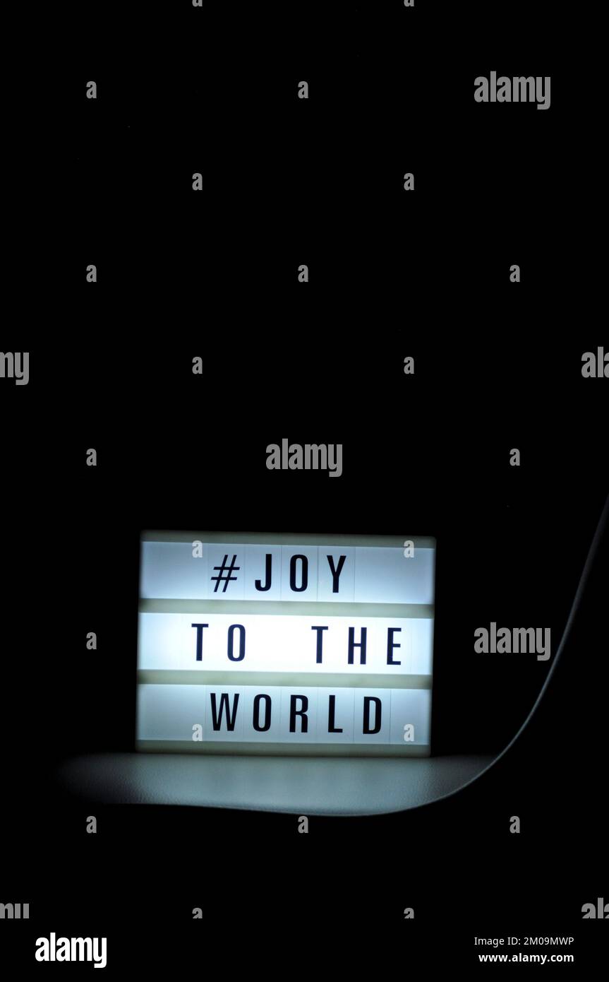 Leuchtkasten mit dem Satz "# Freude an die Welt", beleuchtet in Schatten und dunklem Hintergrund Stockfoto