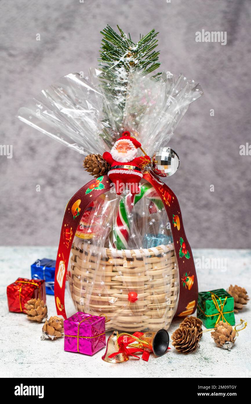 Neujahrsgeschenk. Weihnachtsgeschenk mit Korb auf grauem Hintergrund. Paket mit Schokolade, Nüssen, Snacks Stockfoto