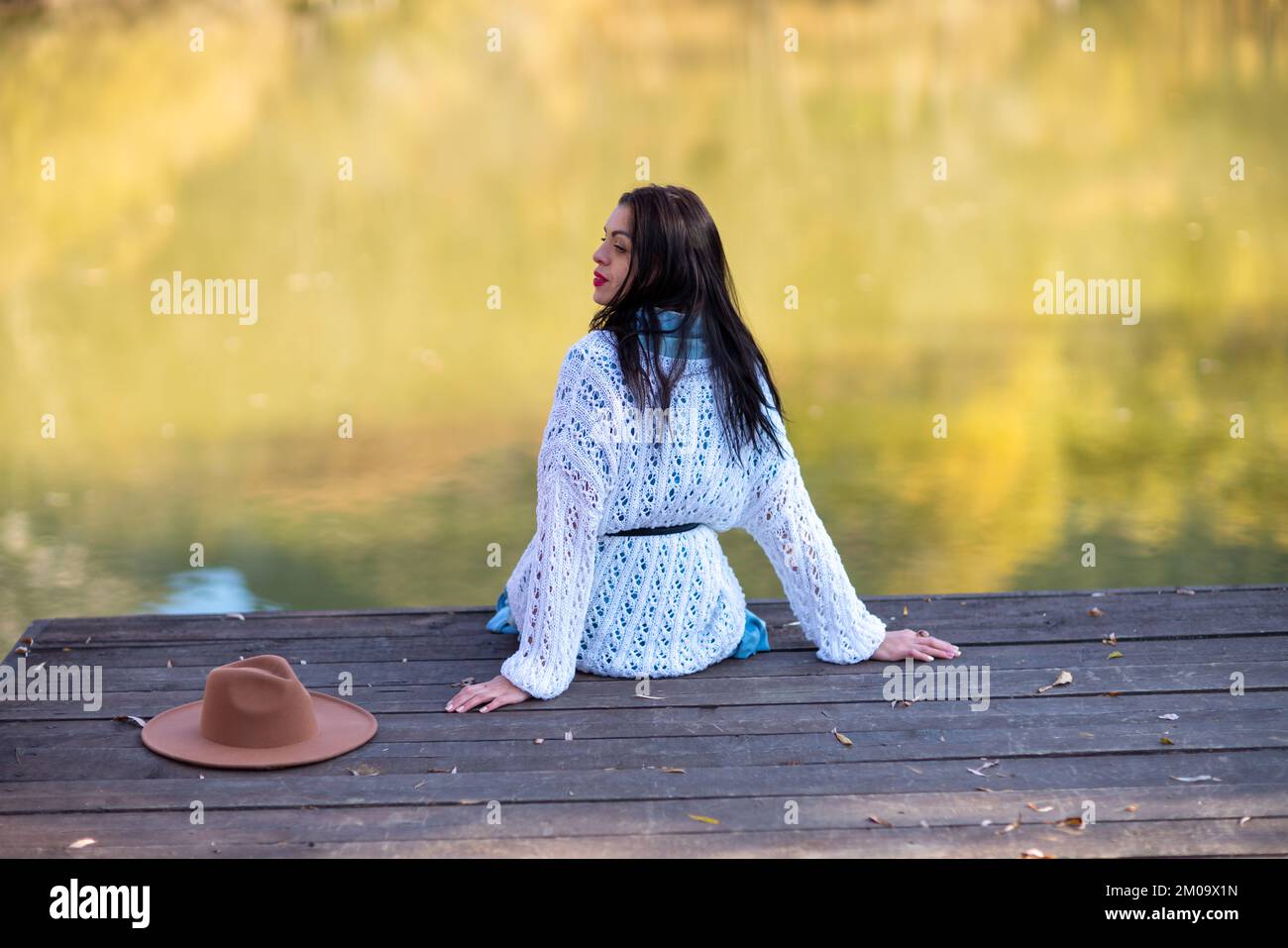 Herbstsee-Frau. Sie sitzt im Herbst an einem Teich auf einem hölzernen Pier und bewundert die Natur. Das Konzept des Tourismus, Wochenenden außerhalb der Stadt. Stockfoto
