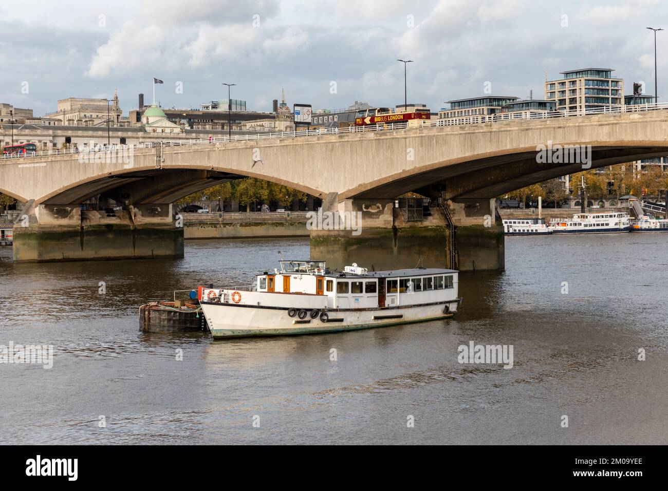 Ein Flussboot auf der Themse segelt unter der Waterloo Bridge, während ein Sightseeing-Bus die Brücke entlang fährt. In der Ferne sind andere Flussboote. Stockfoto