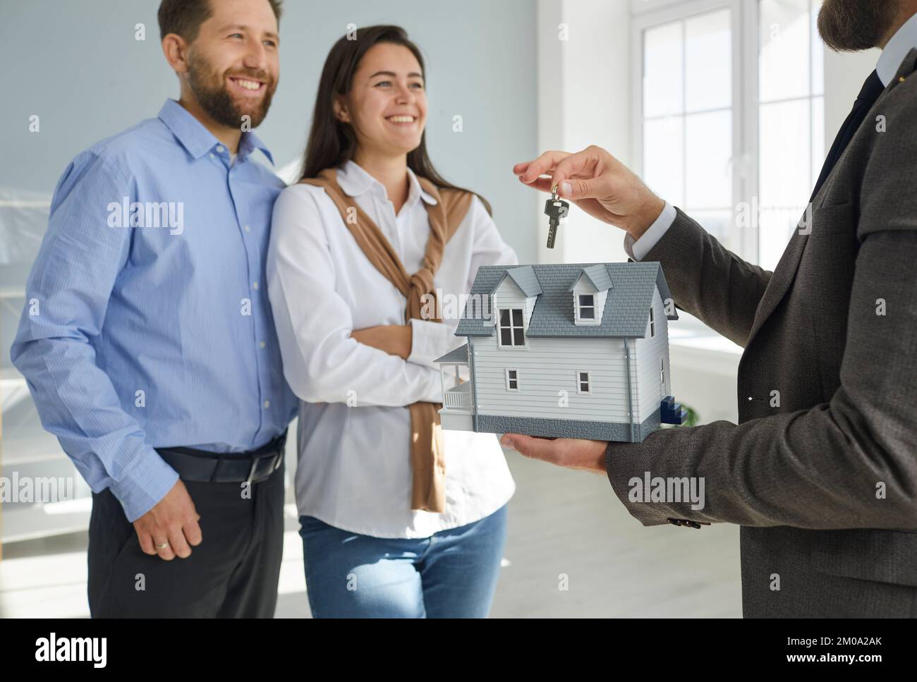 Immobilienmakler übergibt den Schlüssel für ein neues Haus einem glücklichen jungen Familienpaar Stockfoto