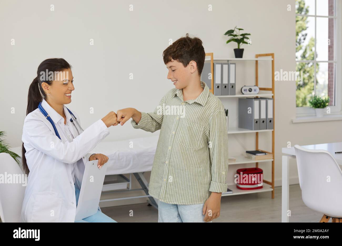 Ein freundlicher Kinderarzt und ein glücklicher kleiner Junge grüßen sich gegenseitig mit einer Faustbrücke Stockfoto
