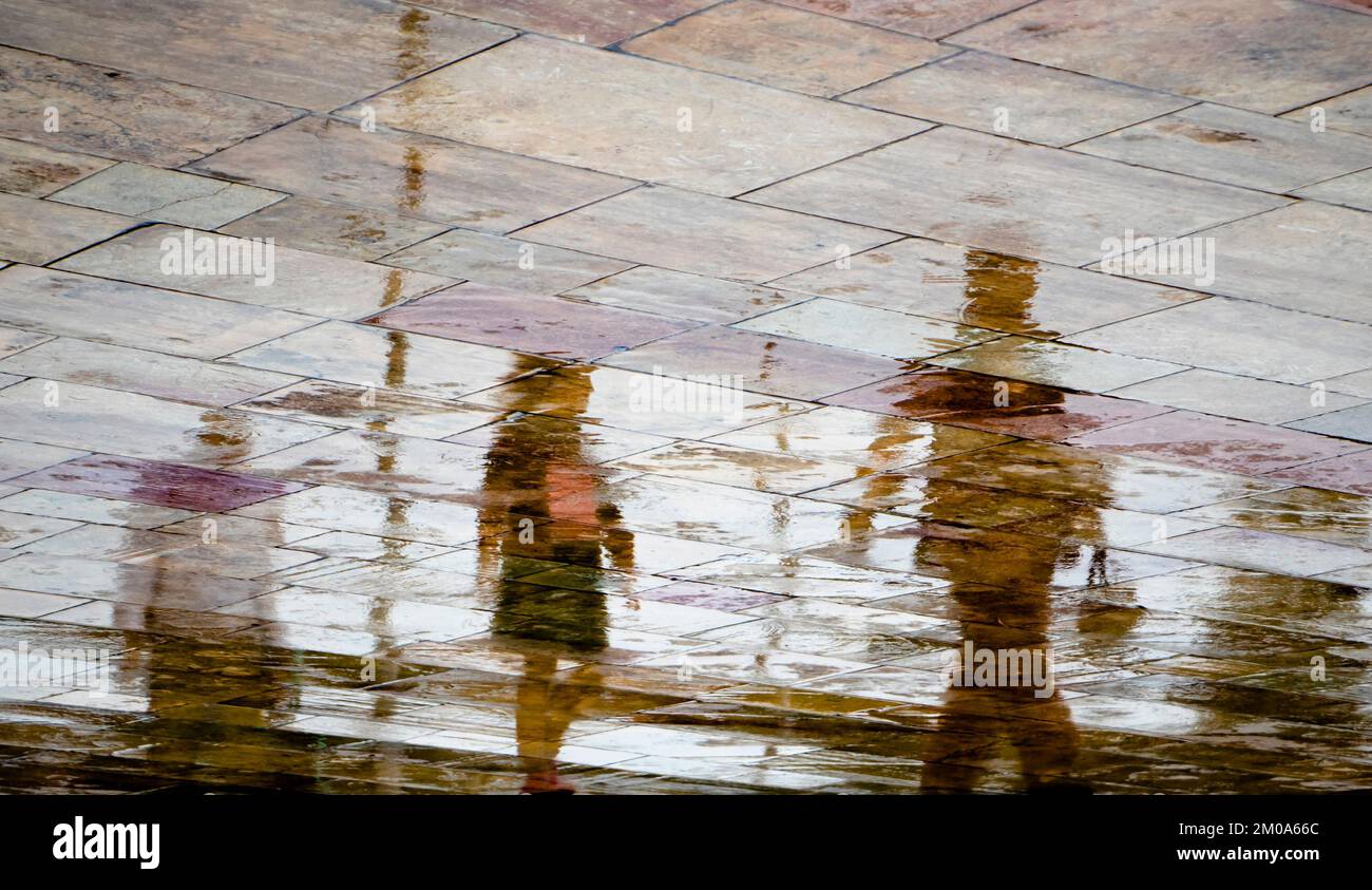 Abstrakte, verschwommene Silhouettenschatten Reflexionen von unbekannten Menschen Reflexionen auf nassen Straßen der Stadt an einem regnerischen Frühlingstag Stockfoto