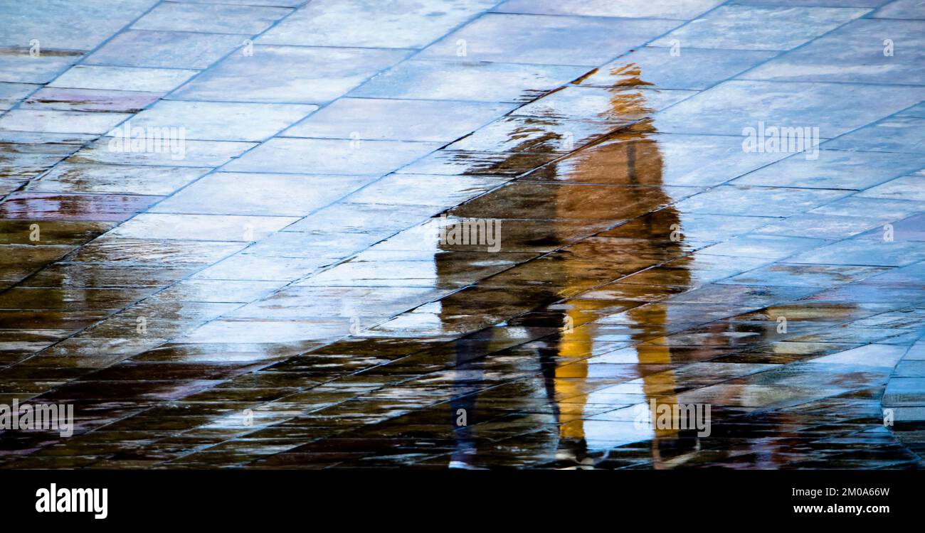 Abstrakte, verschwommene Silhouettenschatten Reflexionen von unbekannten Menschen Reflexionen auf nassen Straßen der Stadt an einem regnerischen Frühlingstag Stockfoto