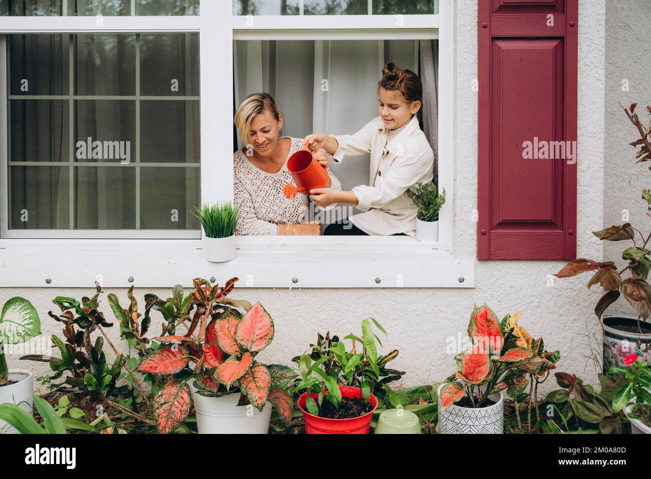 Ein Mädchen mit mom, das Pflanzen aus einer Gießkanne gießt Stockfoto