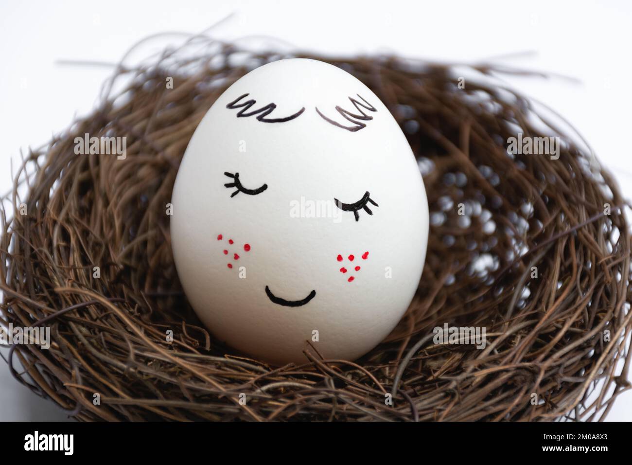 Nahaufnahme eines wunderschönen weißen Eies in einem Weidennest auf weißem Hintergrund. Süßes Gesicht mit roten Sommersprossen. Die Aussicht ist gerade. Eine Frühlings-Postkarte. Frohe Ostern. Stockfoto