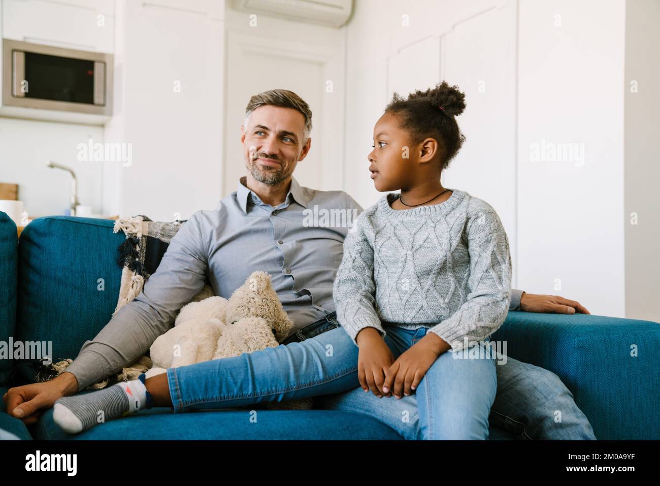 Glücklicher lächelnder Vater, der mit seiner süßen Tochter auf der Couch saß. Einführungskonzept Stockfoto