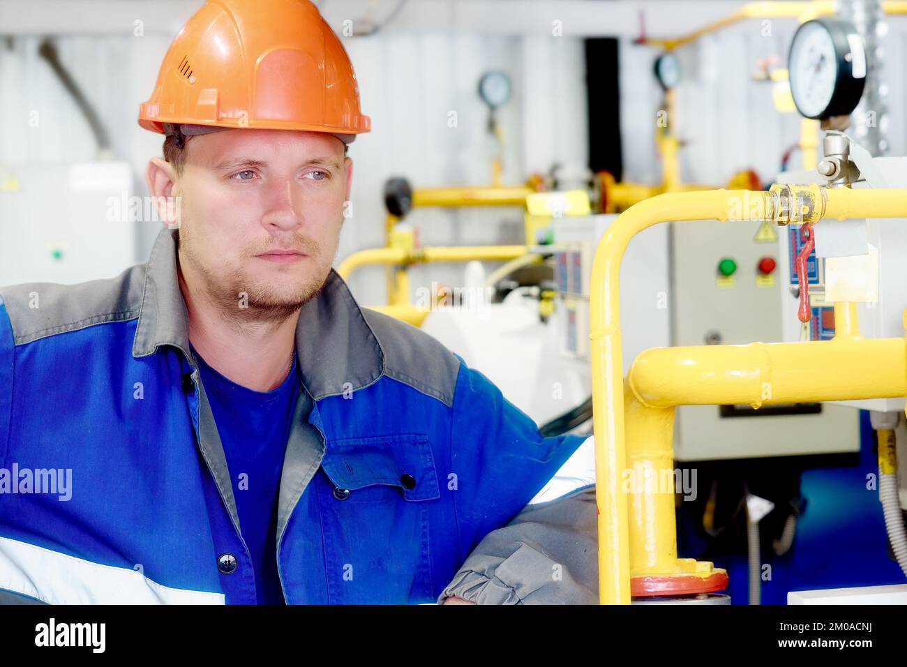 Porträt eines Ingenieurs in Bauhelm und Arbeitskleidung auf industriellem Hintergrund im Innenbereich. Mitarbeiter der Gasindustrie im Kesselraum. Beginn der Heizsaison in Europa... Stockfoto