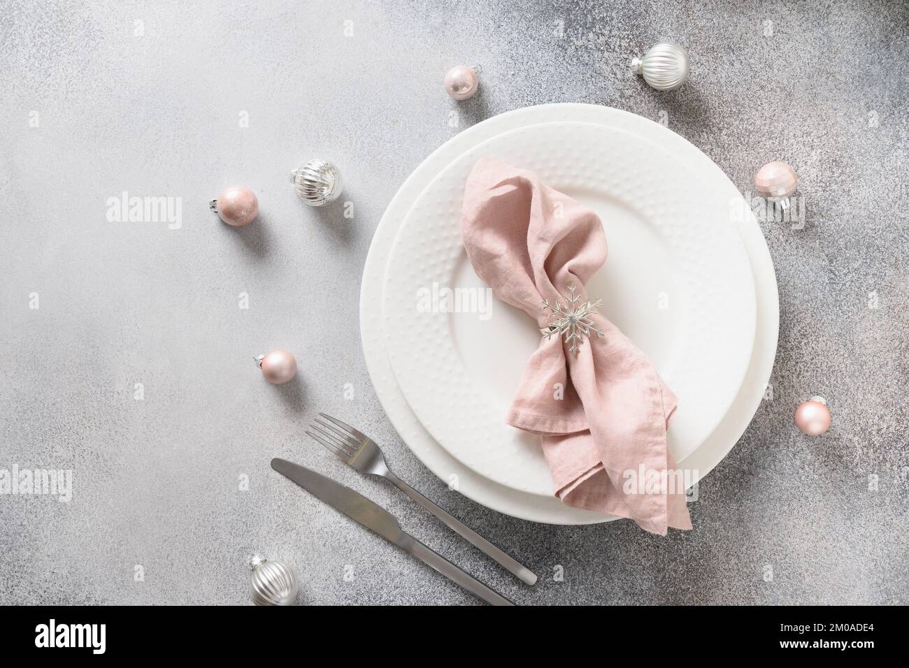 Weihnachtstisch mit weißer Platte, pinkfarbener Kugel und Serviettenring als Schneeflocke auf grauem Hintergrund. Blick von oben. Speicherplatz kopieren. Weihnachtsessen Stockfoto
