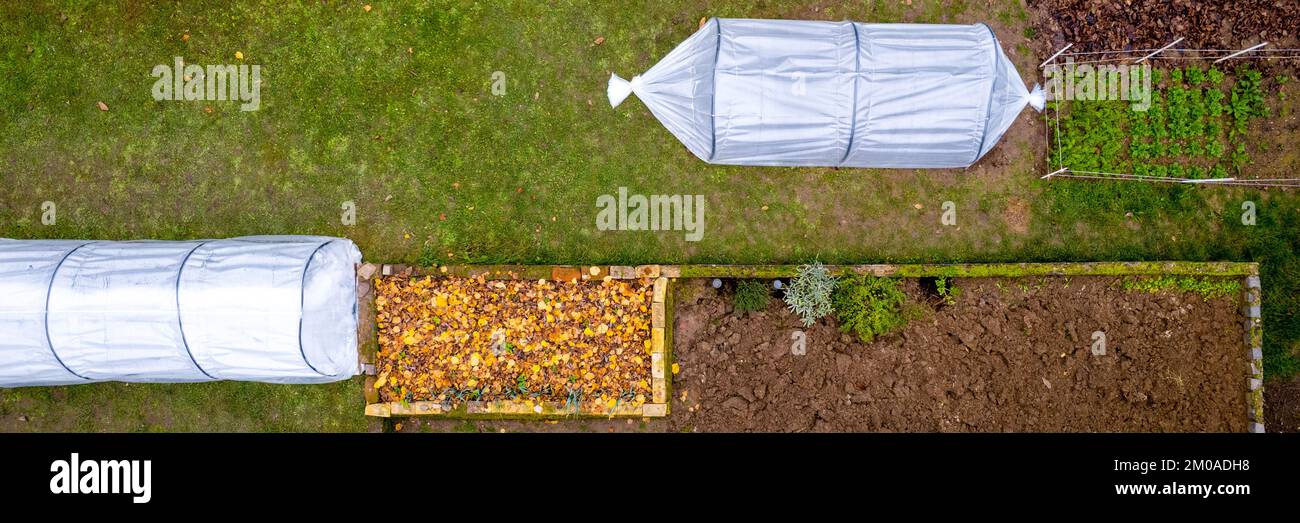 Luftaufnahme von Heimwerker-Tieftunnel-Gewächshäusern in einem Heimgarten. Polytunnel, Herbstgarten, Hintergrund für Schutz vor Kälte. Stockfoto