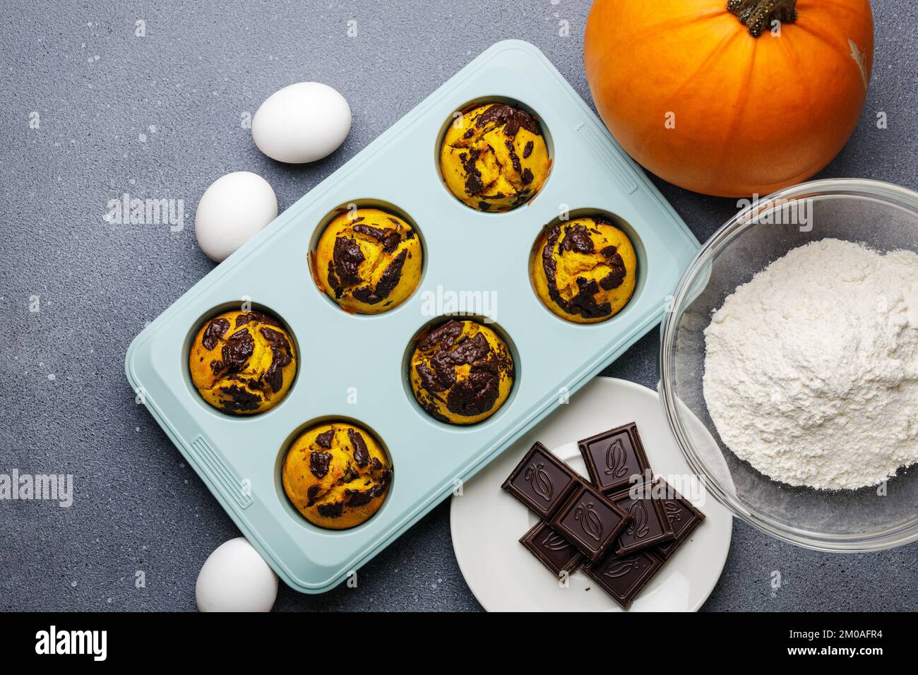 Kürbis-Muffins, gebacken in der Silikonform am Tisch mit Zutaten. Muffin-Bäckerei mit hausgemachtem Kochhintergrund Stockfoto Kürbis-Muffins, gebacken in der Silikonform am Tisch mit Zutaten. Muffin-Bäckerei mit hausgemachtem Kochhintergrund Stockfoto