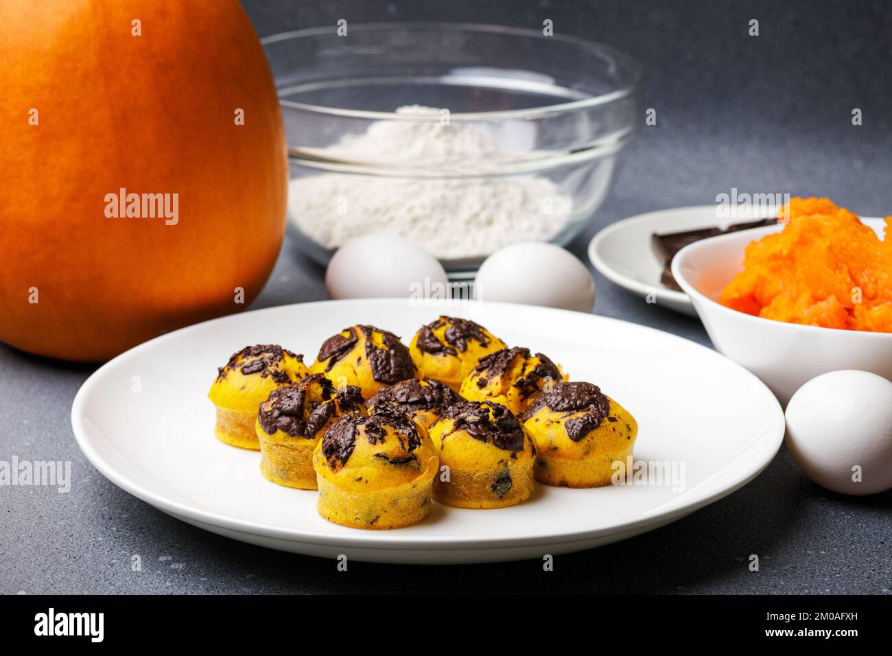 Süße kleine Kürbis-Muffins, serviert am Tisch mit Zutaten. Muffin-Bäckerei mit hausgemachtem Kochhintergrund Stockfoto Süße kleine Kürbis-Muffins, serviert am Tisch mit Zutaten. Muffin-Bäckerei mit hausgemachtem Kochhintergrund Stockfoto