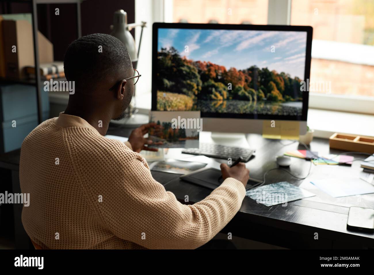 Professioneller Fotograf, der Fotos am Computer am Schreibtisch in seinem Heimbüro bearbeitet Stockfoto