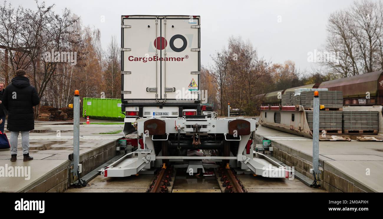 05. Dezember 2022, Sachsen, Leipzig: Ein Mann sieht zu, wie ein Sattelschlepper auf einem Güterbahnhof mit einer neuen Ladetechnik auf einen Eisenbahnwaggon verladen wird. Das Leipziger Unternehmen CargoBeamer möchte den Güterverkehr innerhalb Europas effizienter und umweltfreundlicher gestalten. Im neu entwickelten Terminal können Lkw-Anhänger mit Hilfe einer sogenannten Laderampe seitlich auf den Waggon gefahren werden. Dadurch wird das Problem umgangen, dass fast alle Lkw-Anhänger nicht mit einem Kran angehoben werden können, was die Beladung der Schiene kostspielig und nicht lohnenswert macht. Das erste Terminal des Unternehmens ist in Calais in Nor in Betrieb Stockfoto