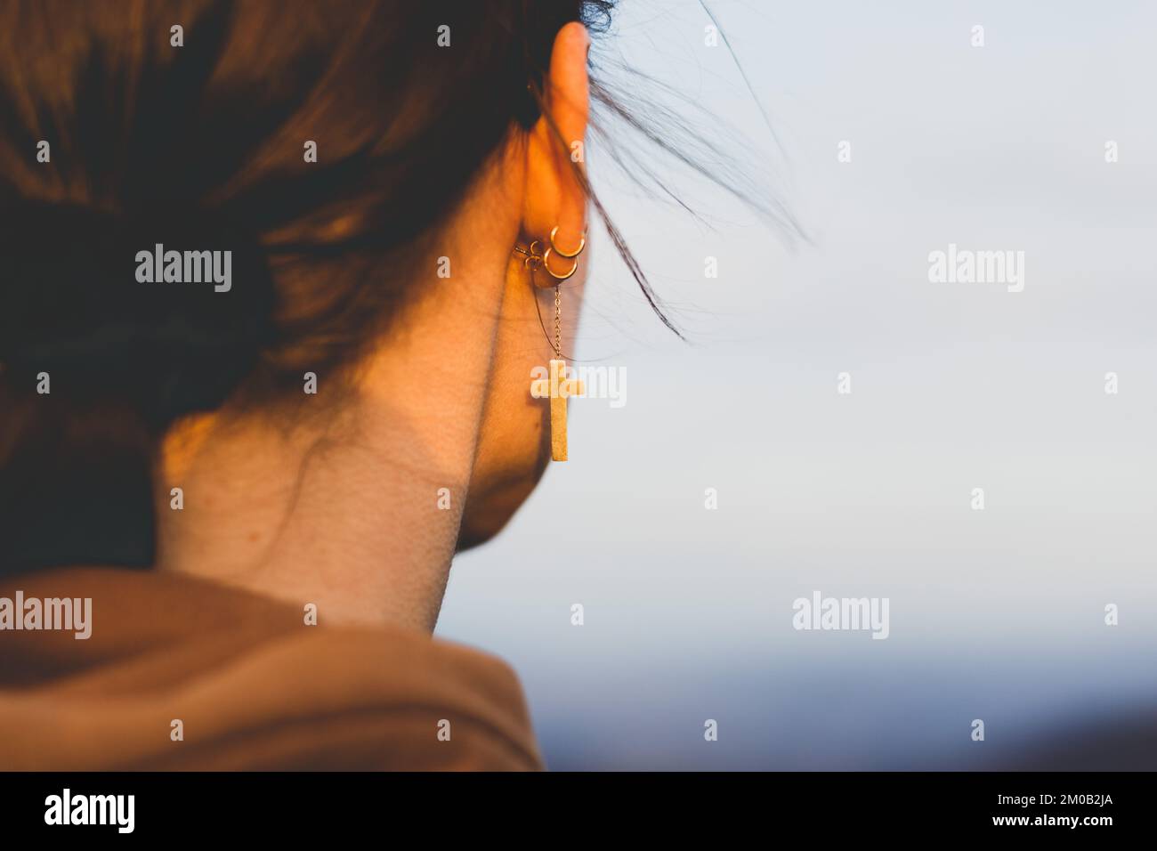 Ein Mädchen mit gekreuzten Ohrringen sieht sich die Landschaft mit dem Himmel im Hintergrund an Stockfoto
