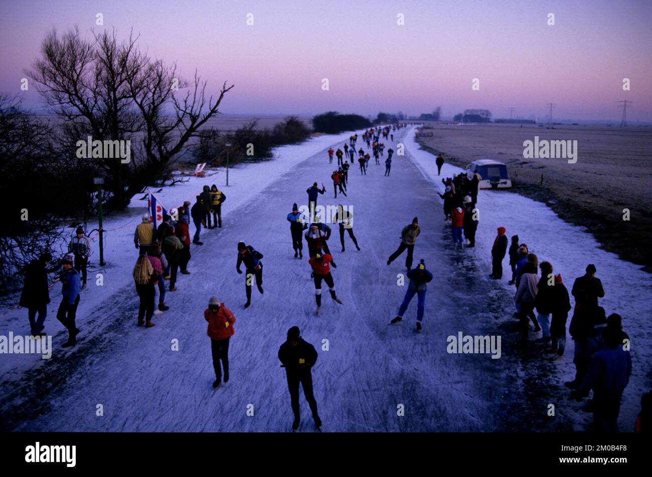 Elfstedentocht Holland Ice Skating Race 1986 die Elfstedentocht auf Englisch die Elf Städte Tour ist eine Langstreckentour auf natürlichem Eis, fast 200 Kilometer (120 Meilen) lang, die sowohl als Speedskating-Wettbewerb (mit 300 Teilnehmern) als auch als Freizeittour (mit 16.000 Skatern) stattfindet. Die Elfstedentocht ist die größte Schlittschuhbahn der Welt. Die Tour findet in der Provinz Friesland im Norden der Niederlande statt und führt vorbei an allen elf historischen Städten der Provinz. Die Tour findet höchstens einmal im Jahr statt, nur wenn das natürliche Eis entlang des gesamten Kurses A ist Stockfoto