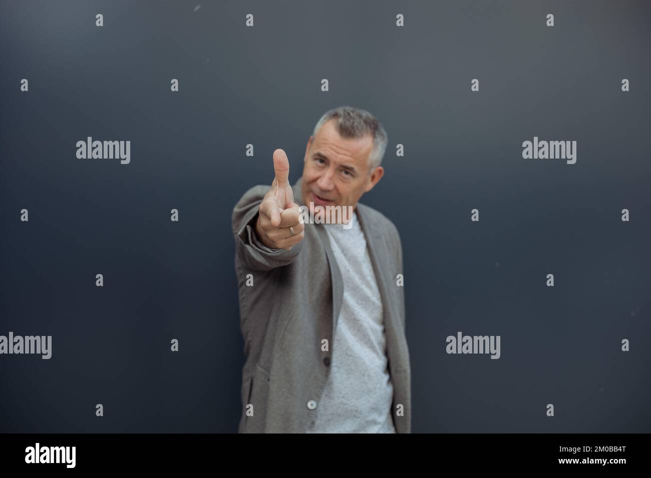 Großaufnahme seriöser, starker, selbstbewusster, grieseliger Mann, der in die Kamera schaut, das Produkt mit dem Zeigefinger vor der Kamera präsentiert Stockfoto