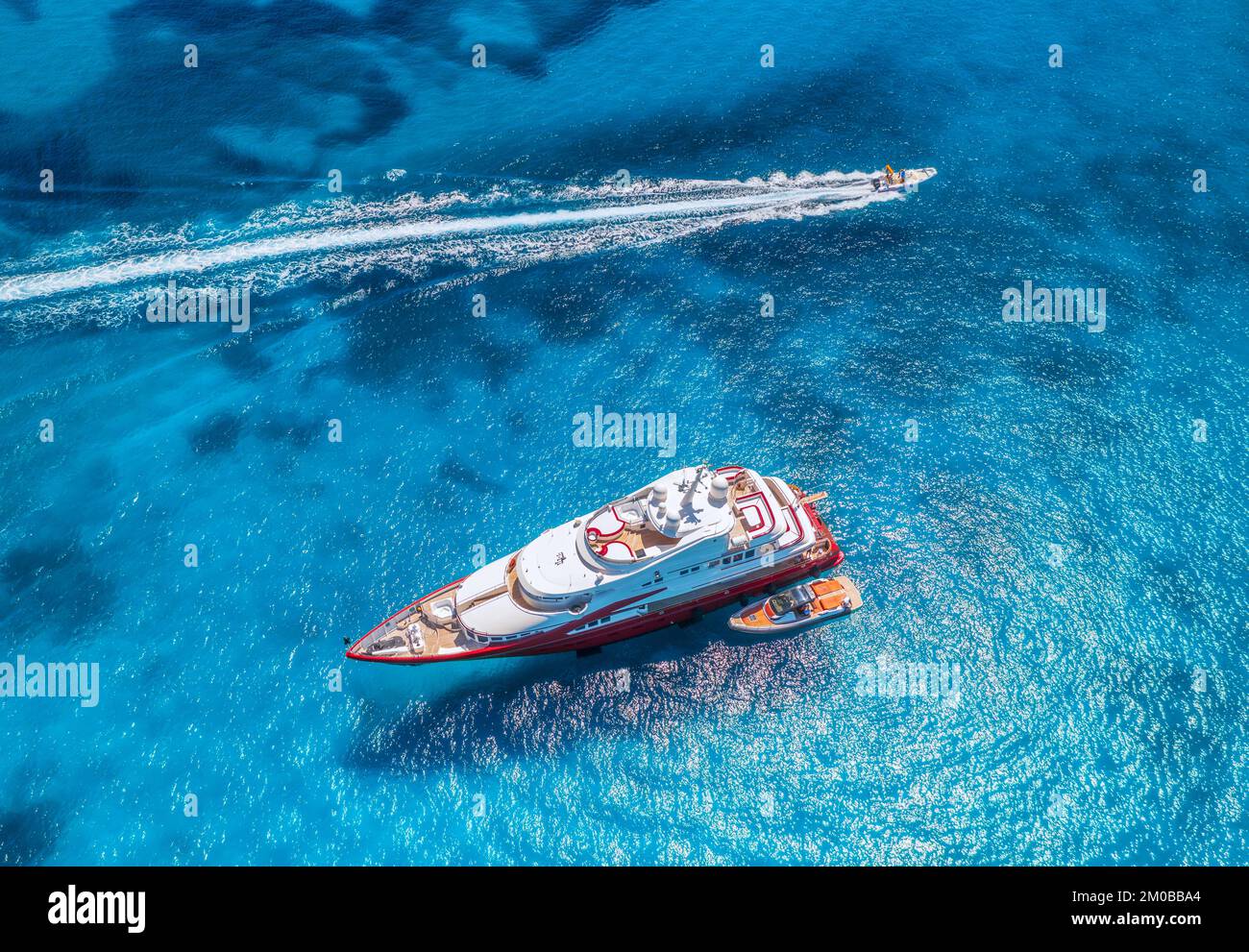 Blick aus der Vogelperspektive auf die wunderschöne rote Luxusyacht und das Boot im blauen Meer bei Sonnenuntergang im Sommer. Insel Sardinien, Italien. Blick von oben auf Schnellboot, Küste, Transpa Stockfoto Blick aus der Vogelperspektive auf die wunderschöne rote Luxusyacht und das Boot im blauen Meer bei Sonnenuntergang im Sommer. Insel Sardinien, Italien. Blick von oben auf Schnellboot, Küste, Transpa Stockfoto