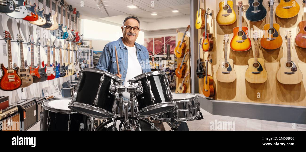 Zwangloser reifer Mann, der Trommeln in einem Musikladen probiert Stockfoto