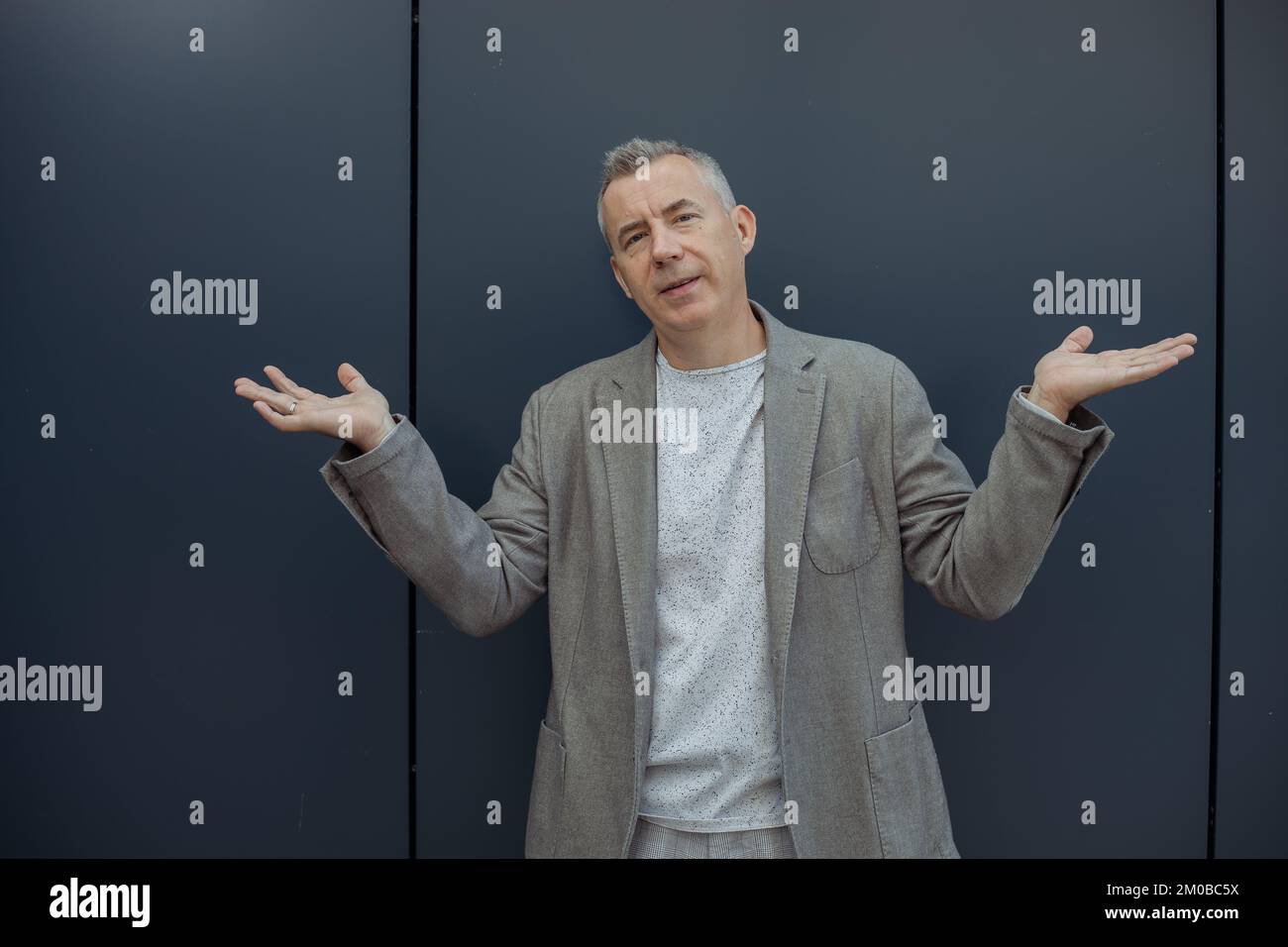 Nahaufnahme ernst, stark, selbstbewusst, grizzliger Mann, der Hände verteilt, in die Kamera schaut, weiß nicht, was man gegen die blaue Wand tun soll Stockfoto