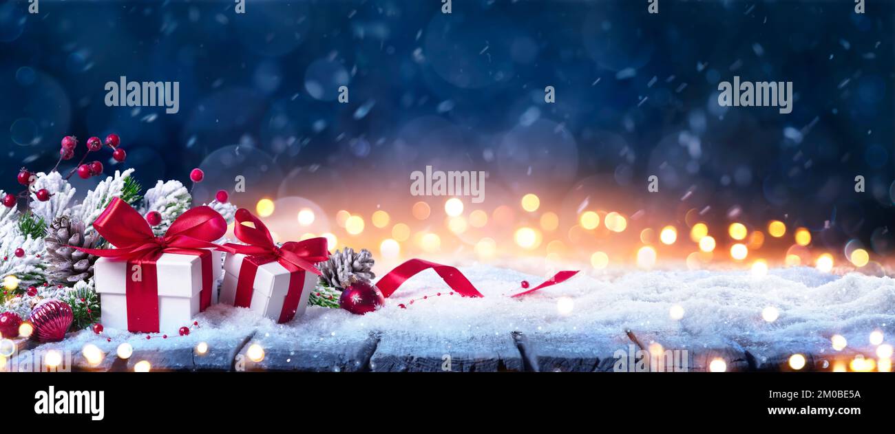 Geschenkbox Auf Schnee Im Winterblauen Hintergrund – Weihnachtsgeschenke Und Rote Dekoration In Verschneiter Nacht Mit Abstrakten Unschärfe-Bokeh-Lichtern Stockfoto