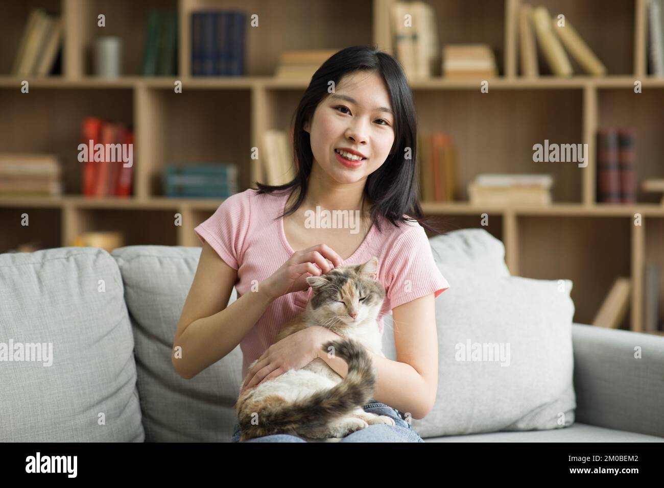 Porträt einer glücklichen asiatischen Dame, die Zeit mit ihrer Katze zu Hause verbringt, auf dem Sofa sitzt und vor der Kamera lächelt Stockfoto