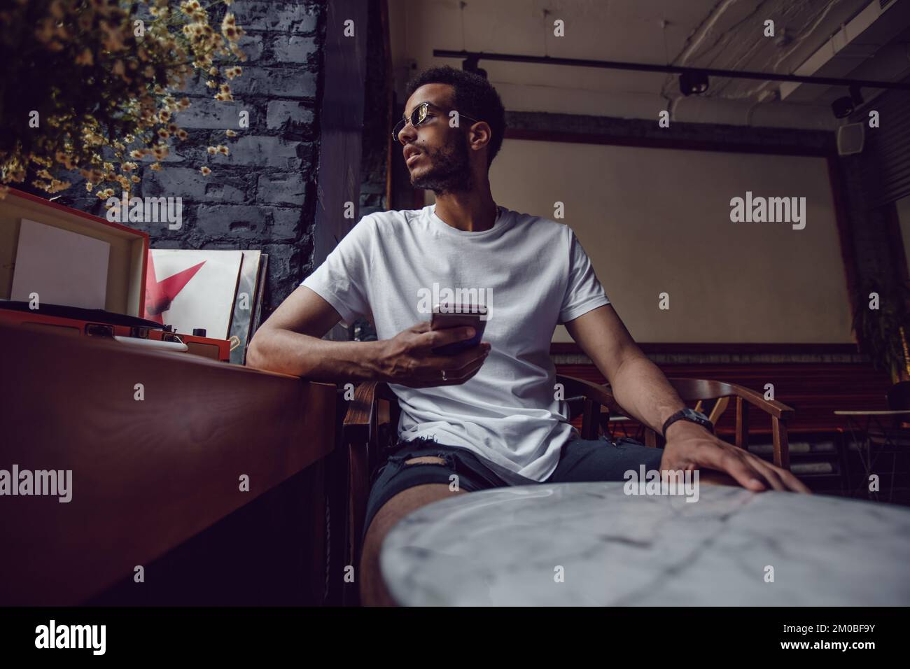 Ein afroamerikaner in einem weißen T-Shirt sitzt in einem Café und telefoniert. Modell. Stockfoto