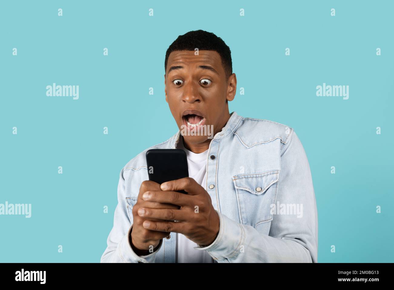 Verängstigter junger afroamerikanischer Typ, ungezwungen, mit offenem Mund und Schrei, schau, am Telefon Stockfoto