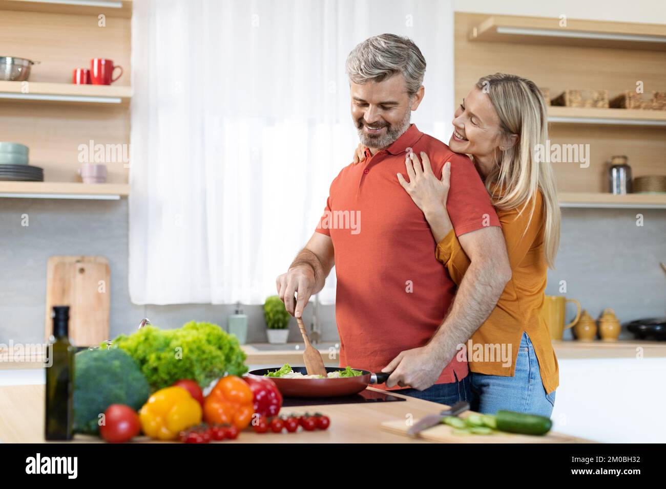 Glückliche, dankbare Frau, die ihren Mann von hinten umarmt, Kücheneinrichtung Stockfoto