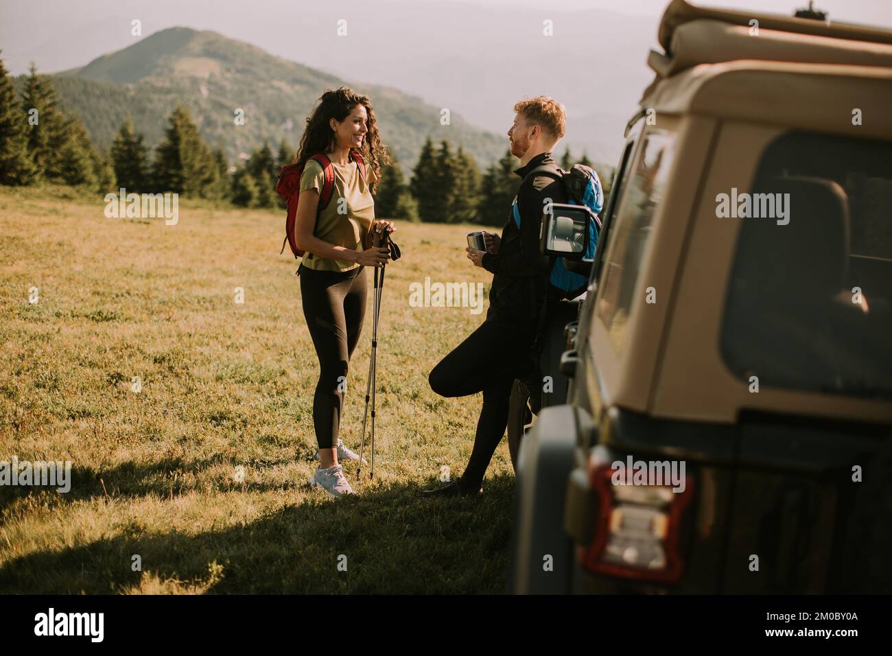 Lächelndes junges Paar bereitet Wanderabenteuer mit Rucksäcken von Geländewagen vor Stockfoto
