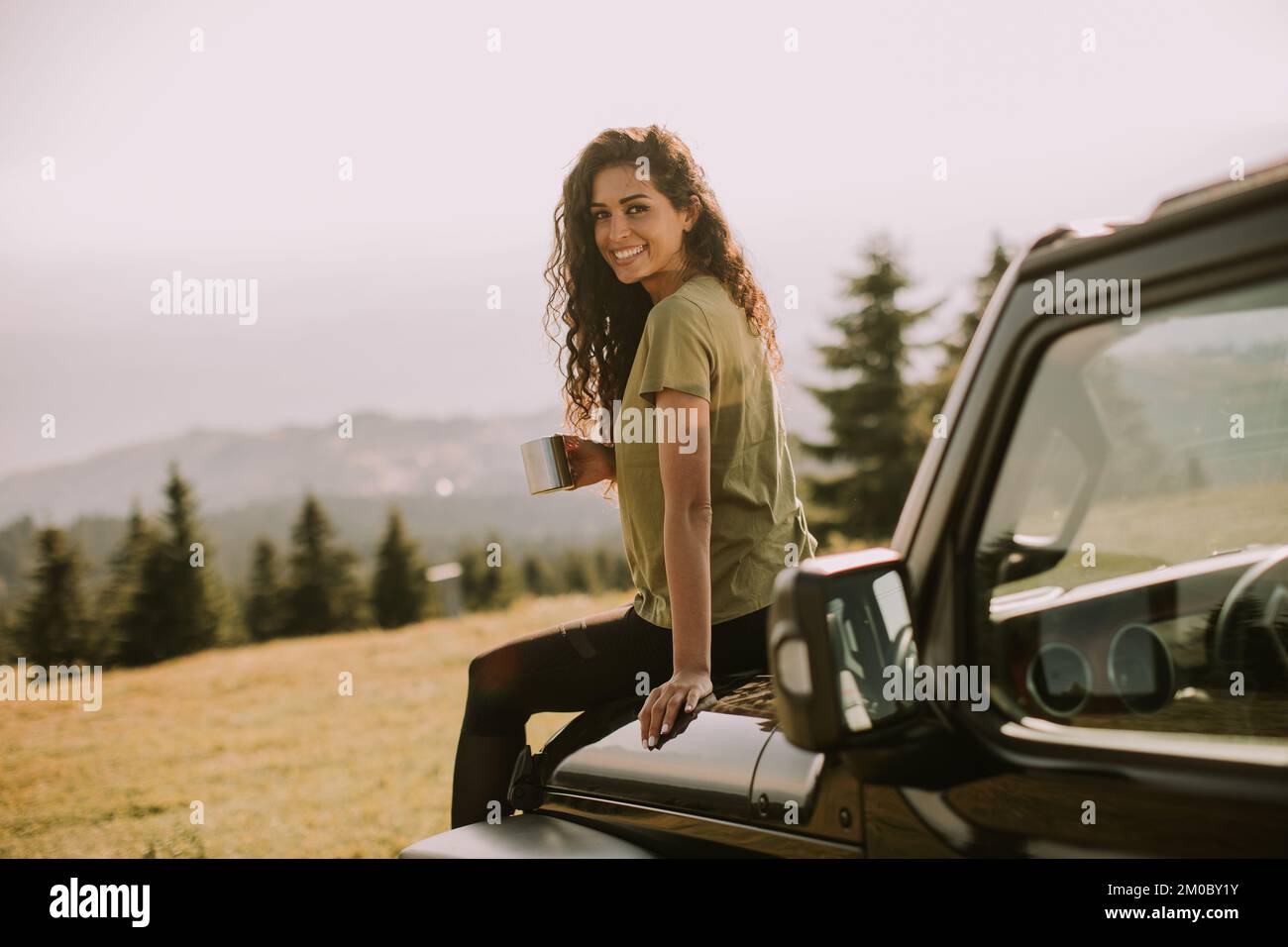 Hübsche junge Frau, die sich auf einer Geländewagenhaube auf dem Land entspannt Stockfoto