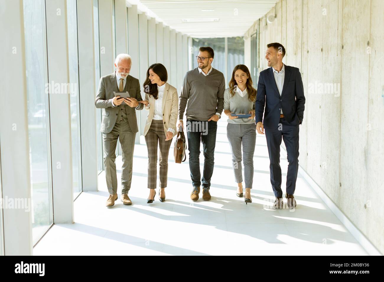 Eine Gruppe von Geschäftsleuten, die an einem sonnigen Tag durch den Büroflur spazieren Stockfoto