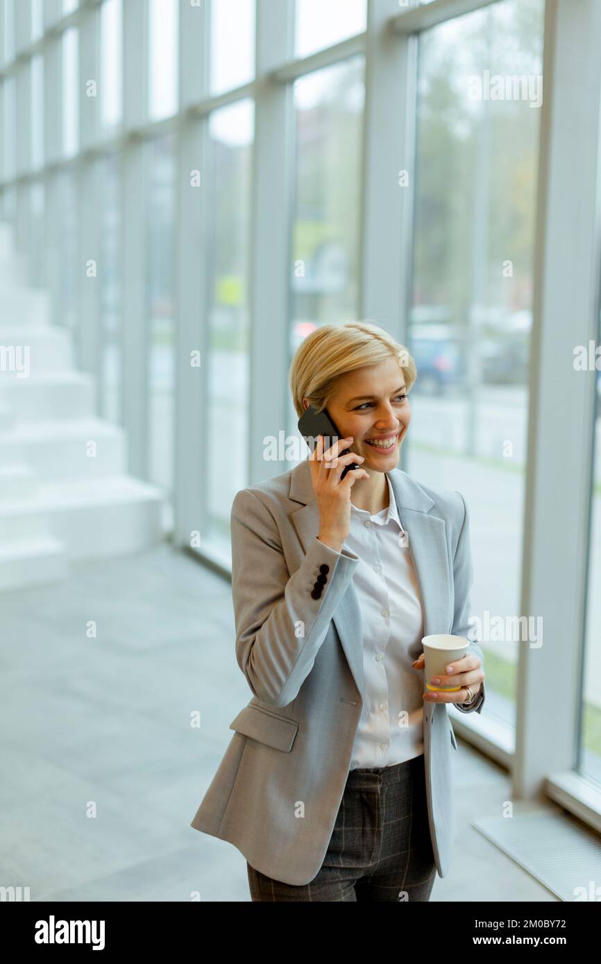 Eine Geschäftsfrau, die ihr Handy benutzt, während sie auf dem modernen Büroflur spaziert Stockfoto