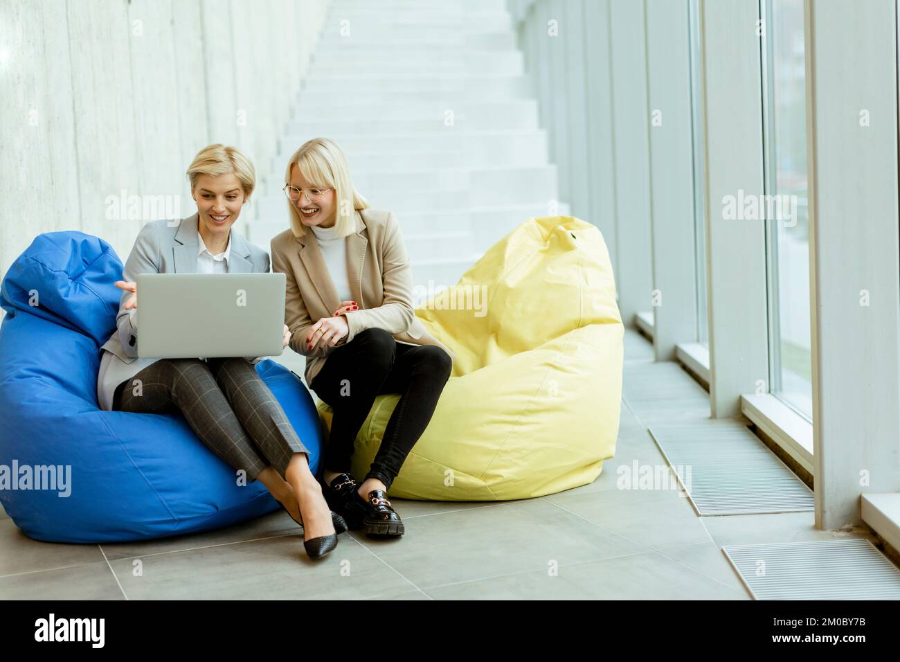 Zwei Geschäftsfrauen, die in einem modernen Büro an einem Laptop mit faulen Taschen arbeiten Stockfoto