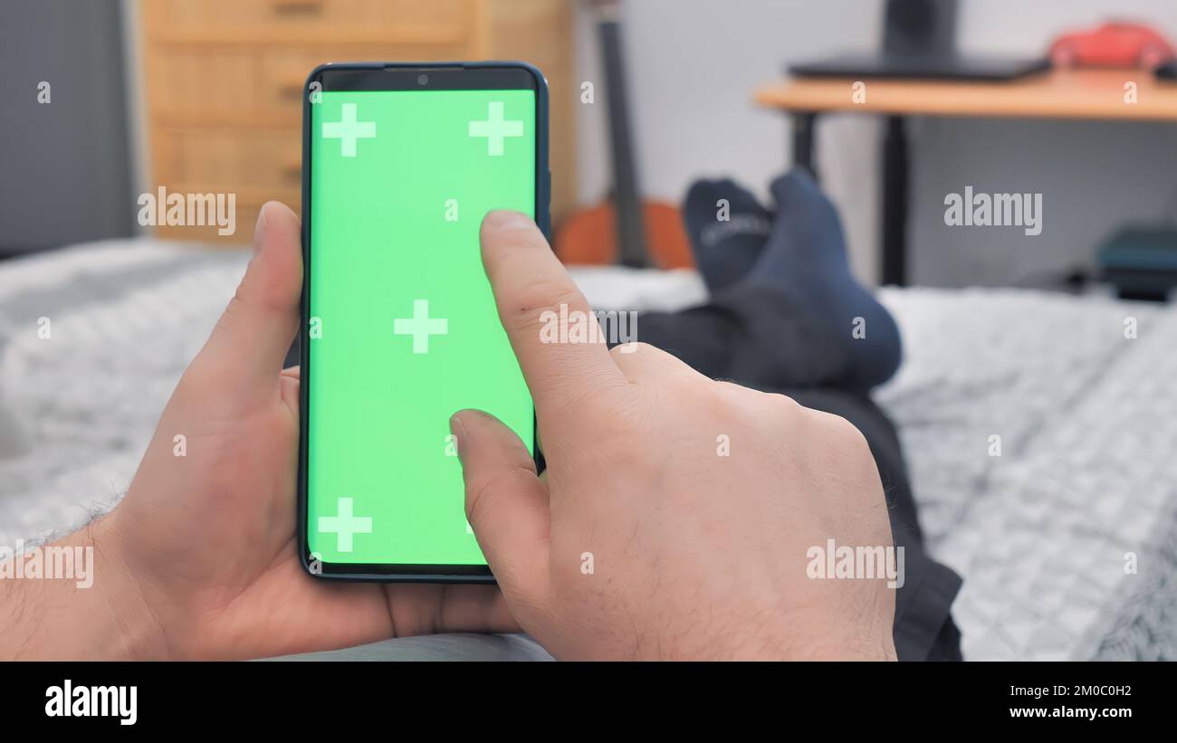 Ein Mann, der nachts auf dem Sofa lag und ein Smartphone mit einem grünen Bildschirm mit Chroma Key benutzte Stockfoto