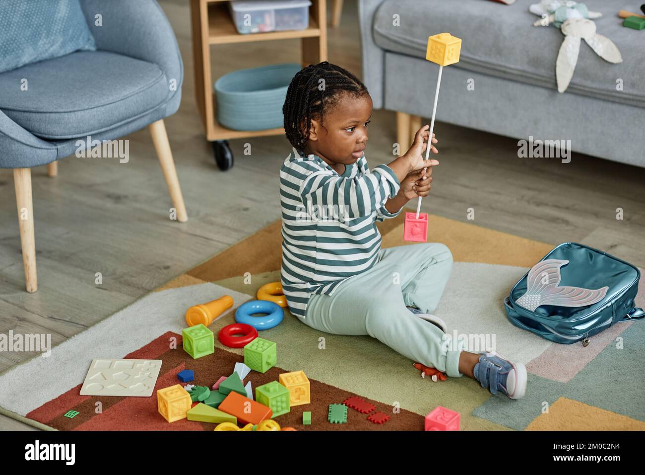 Porträt des süßen schwarzen Babys, das mit Spielzeugen auf dem Teppich spielt, in gemütlichen Wohnungen, Kopierbereich Stockfoto