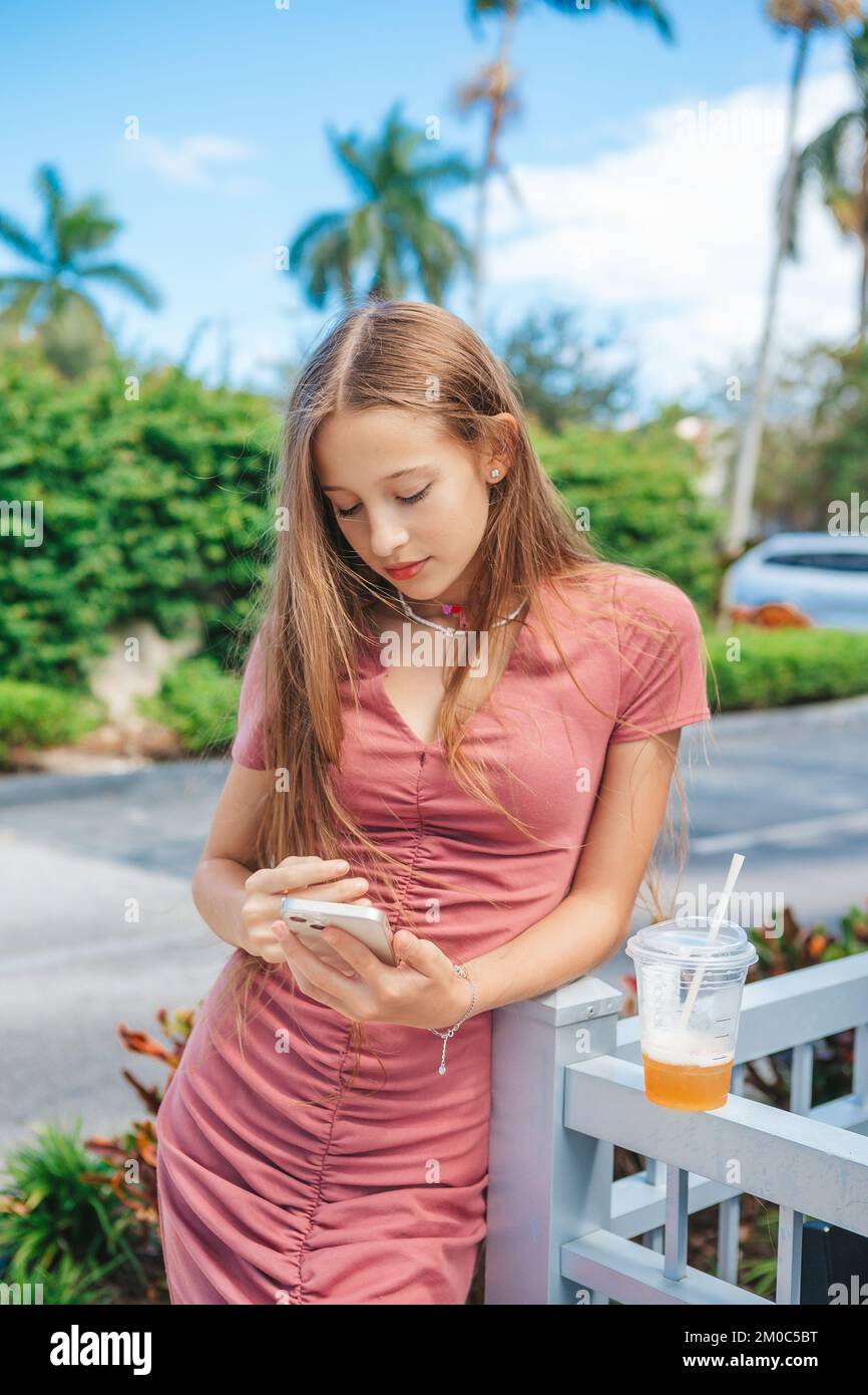 Ein wunderschönes Teenager-Mädchen, das ein Smartphone benutzt und draußen ein Getränk zum Mitnehmen trinkt Stockfoto
