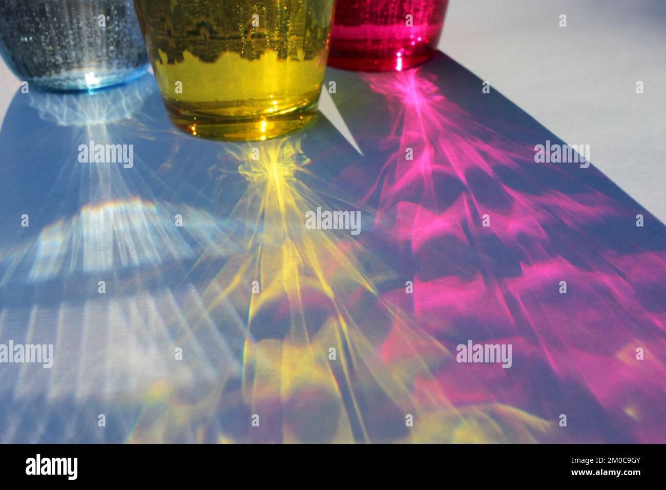 Glitzernde farbige Gläser Wasser auf blauem Hintergrund im Sonnenlicht. Sonnenlicht durch Glas Wasser. Lange harte Schatten. Konzept für Sommerferien. Stockfoto