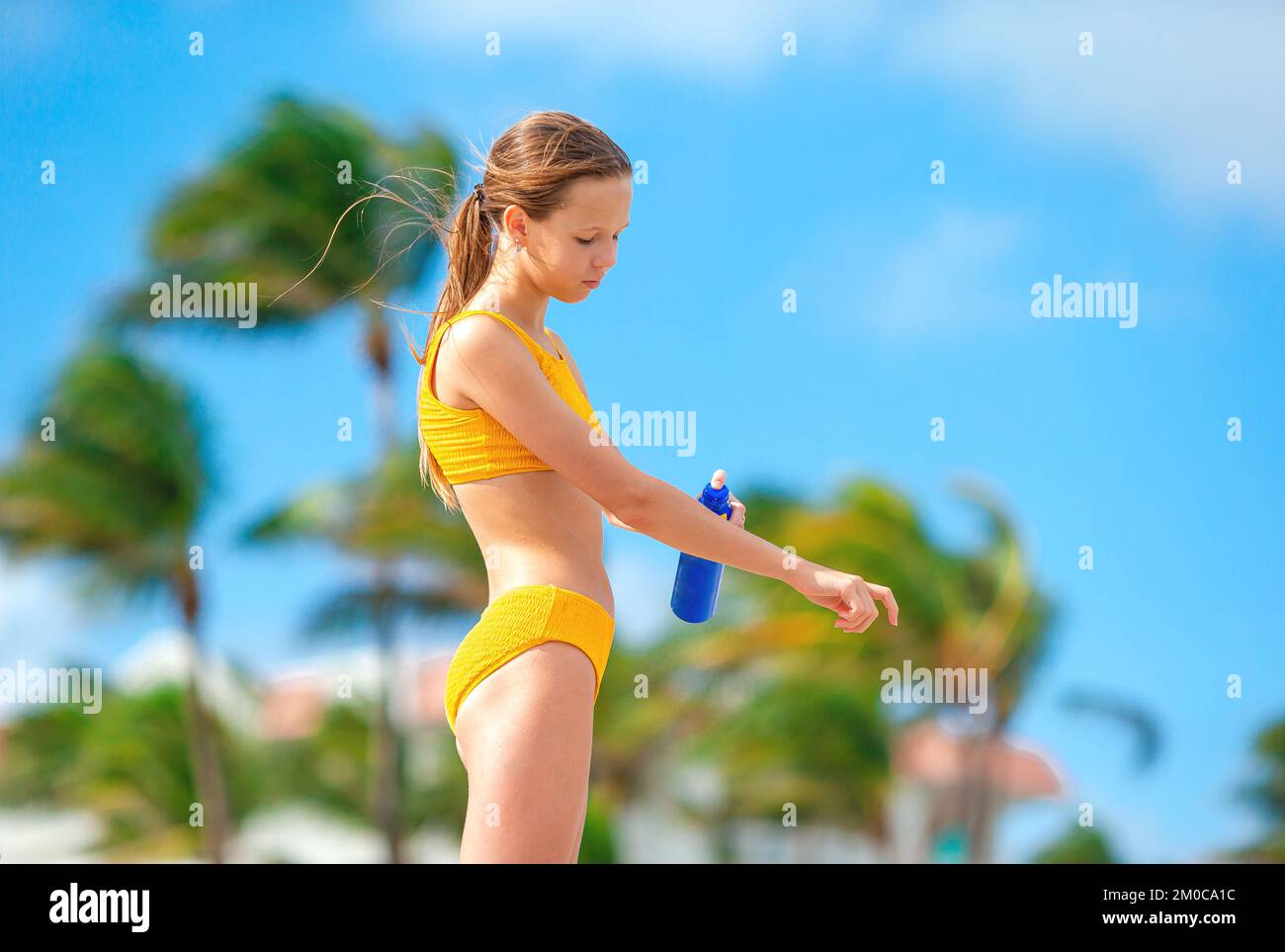 Kleines Mädchen mit Flasche Sonnencreme am tropischen Strand sitzen Stockfoto