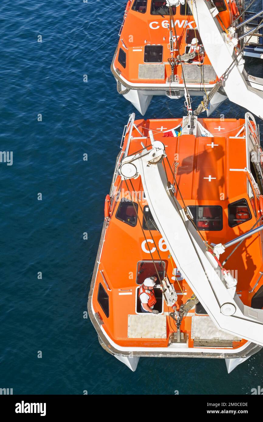 Argostili, Griechenland - Juni 2022: Besatzungsmitglied, das auf einem Rettungsboot arbeitet, um es auf einem Kreuzfahrtschiff abzusenken und Passagiere an Land zu bringen, um die Stadt zu besuchen Stockfoto