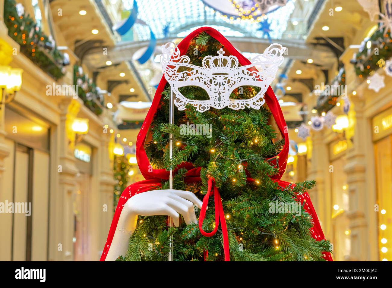Weihnachtsbaum in einem roten Umhang mit einer Kapuze und einer offenen Maskenmaske in ihrer Hand. Stockfoto