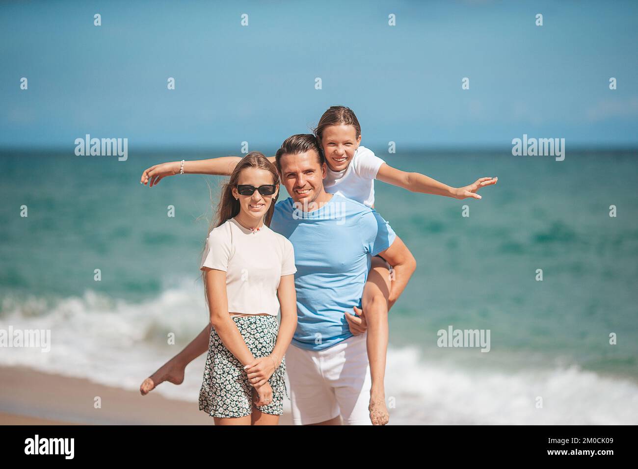 Porträt eines Vaters mit seinen liebenswerten Töchtern am Strand während ihres Sommerurlaubs Stockfoto