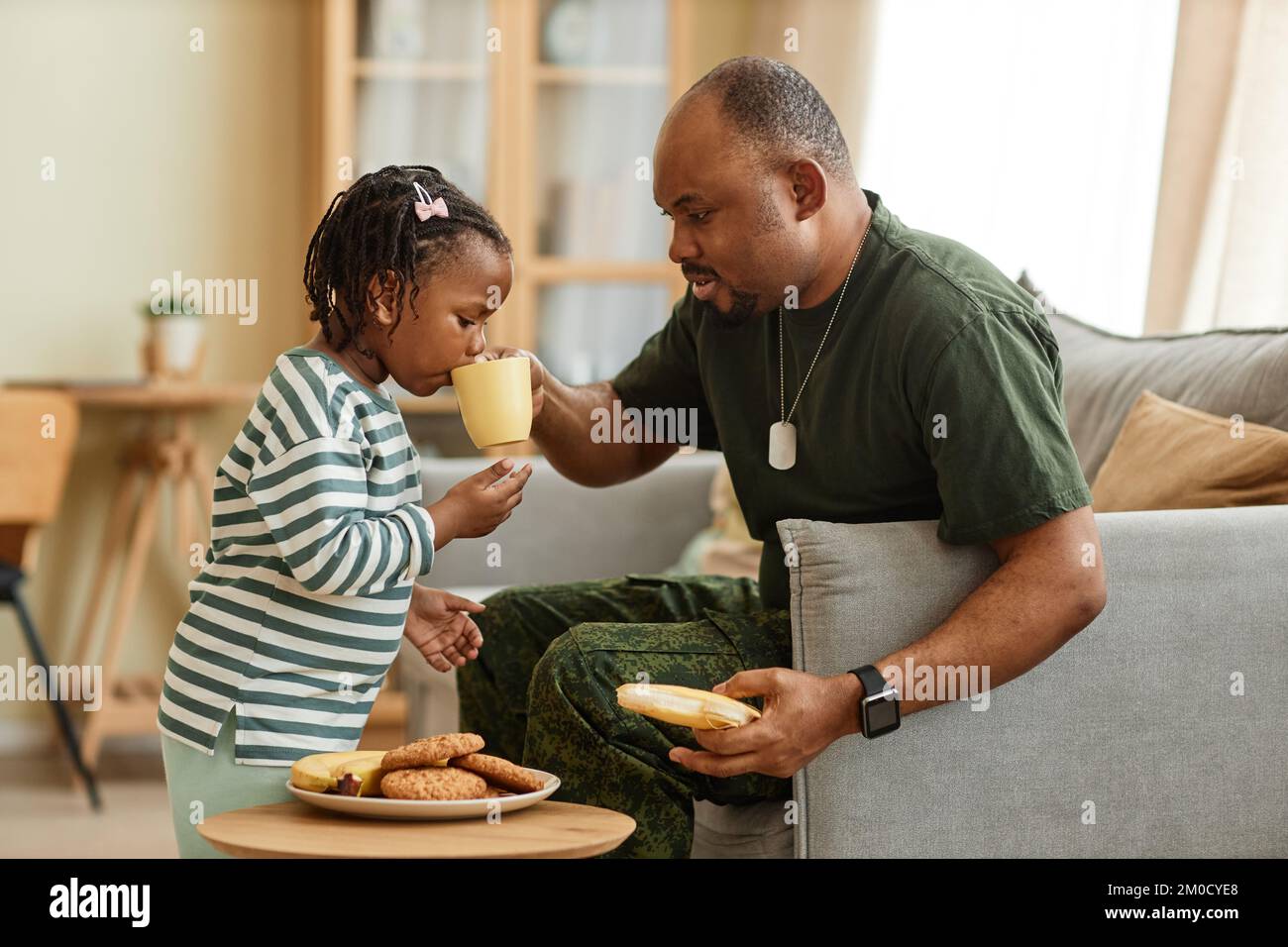 Seitliches Porträt eines fürsorglichen schwarzen Vaters, der Tee und Kekse mit seiner süßen Tochter teilt Stockfoto