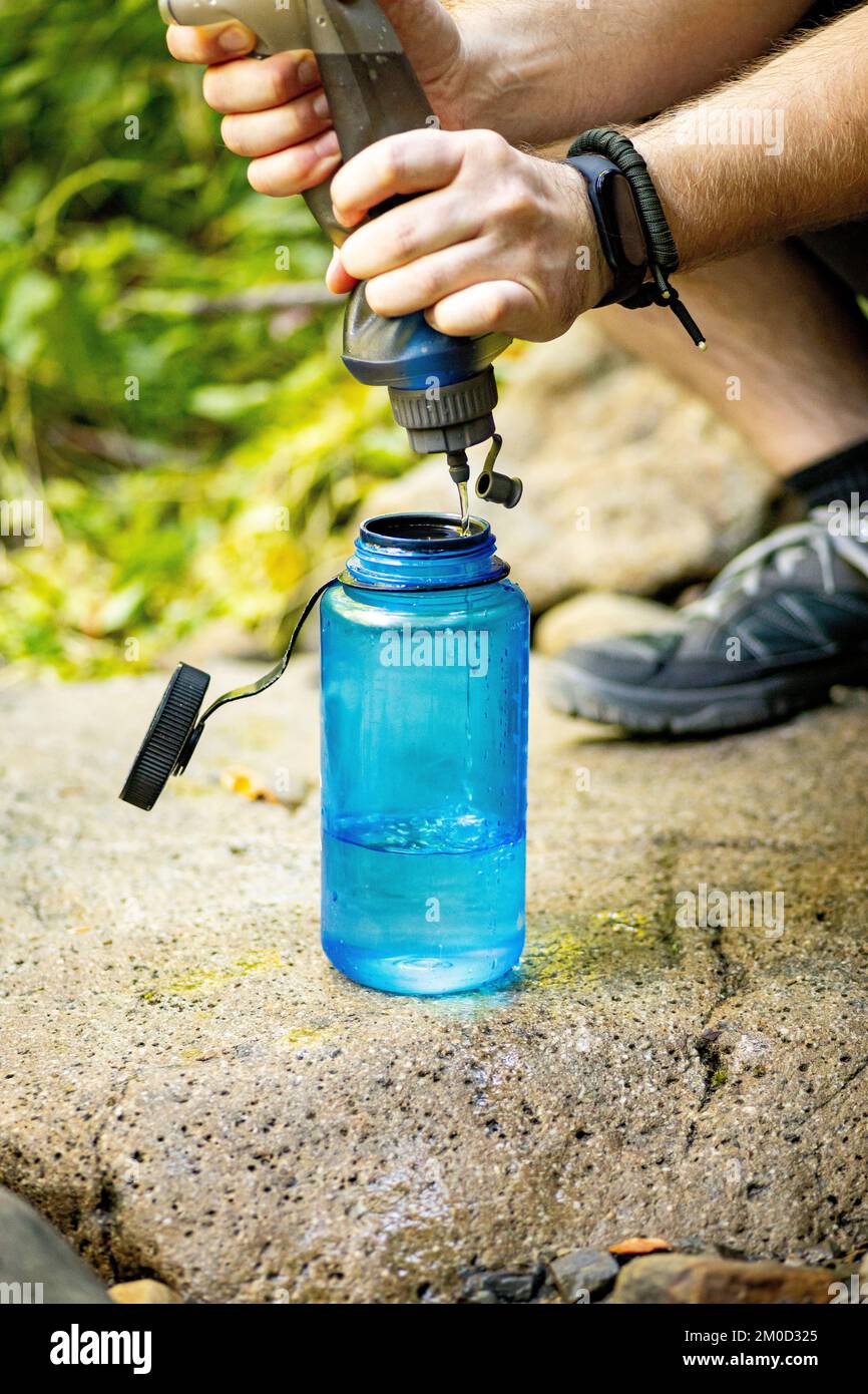 Eine Nahaufnahme der Hände eines Wanderer, der Wasser in eine blaue Weithalsflasche auf einem Felsen in freier Wildbahn drückt Stockfoto Eine Nahaufnahme der Hände eines Wanderer, der Wasser in eine blaue Weithalsflasche auf einem Felsen in freier Wildbahn drückt Stockfoto
