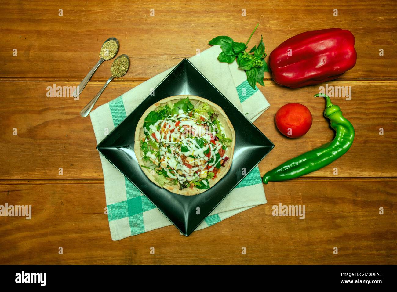 Ein Salat mit Gemüse und viel Soße auf einem Pizzabrot auf einem schwarzen Teller Stockfoto