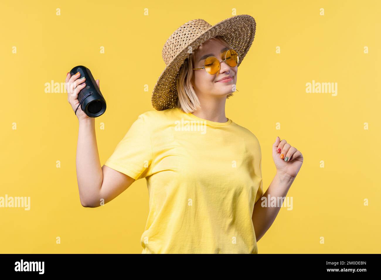 Lady tanzt, genießt den gelben Studiohintergrund. Sie bewegt sich zum Rhythmus der Musik. Junge Frau, die Musik über kabellose tragbare Lautsprecher hört – modern Stockfoto