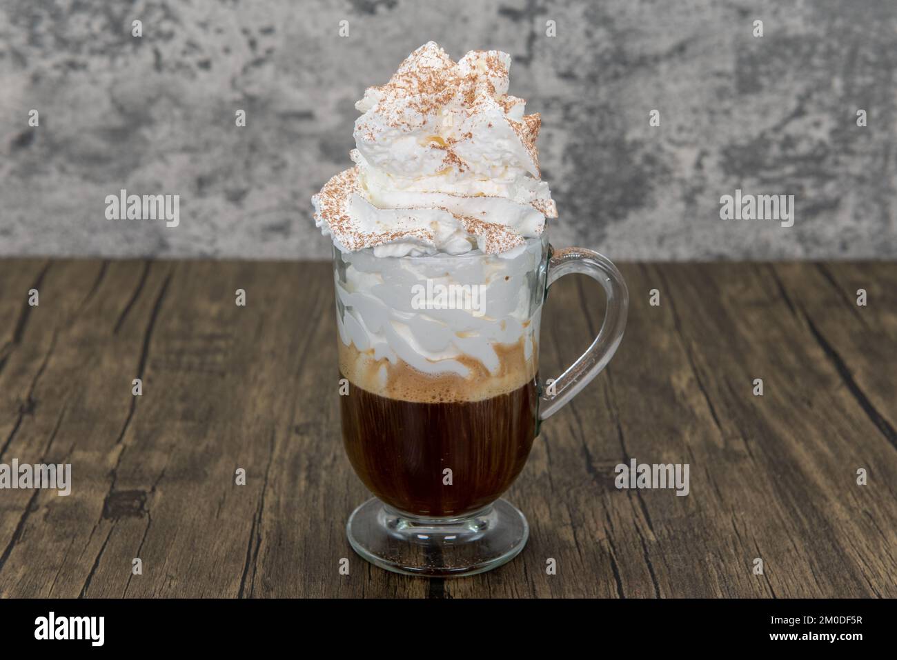 Dunkel gerösteter, starker Kaffee mit süßer Schlagsahne in einer klaren Tasse als energiegeladenes Morgengetränk. Stockfoto