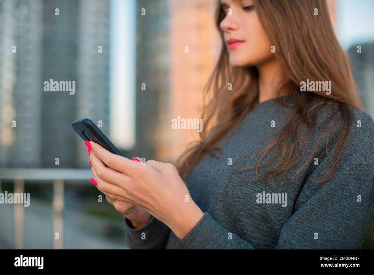 Nahaufnahme junge Frau, die ein Smartphone auf der Straße vor dem Hintergrund von Gebäuden hält, Hände bei der Arbeit mit digitaler Technologie Stockfoto