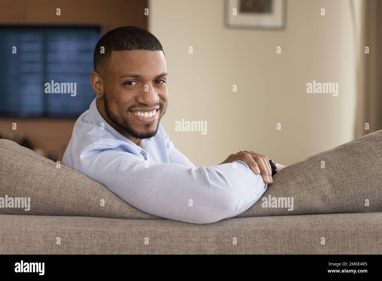 Glücklicher, gutaussehender, junger, schwarzer Hausbesitzer, der auf der Couch sitzt Stockfoto